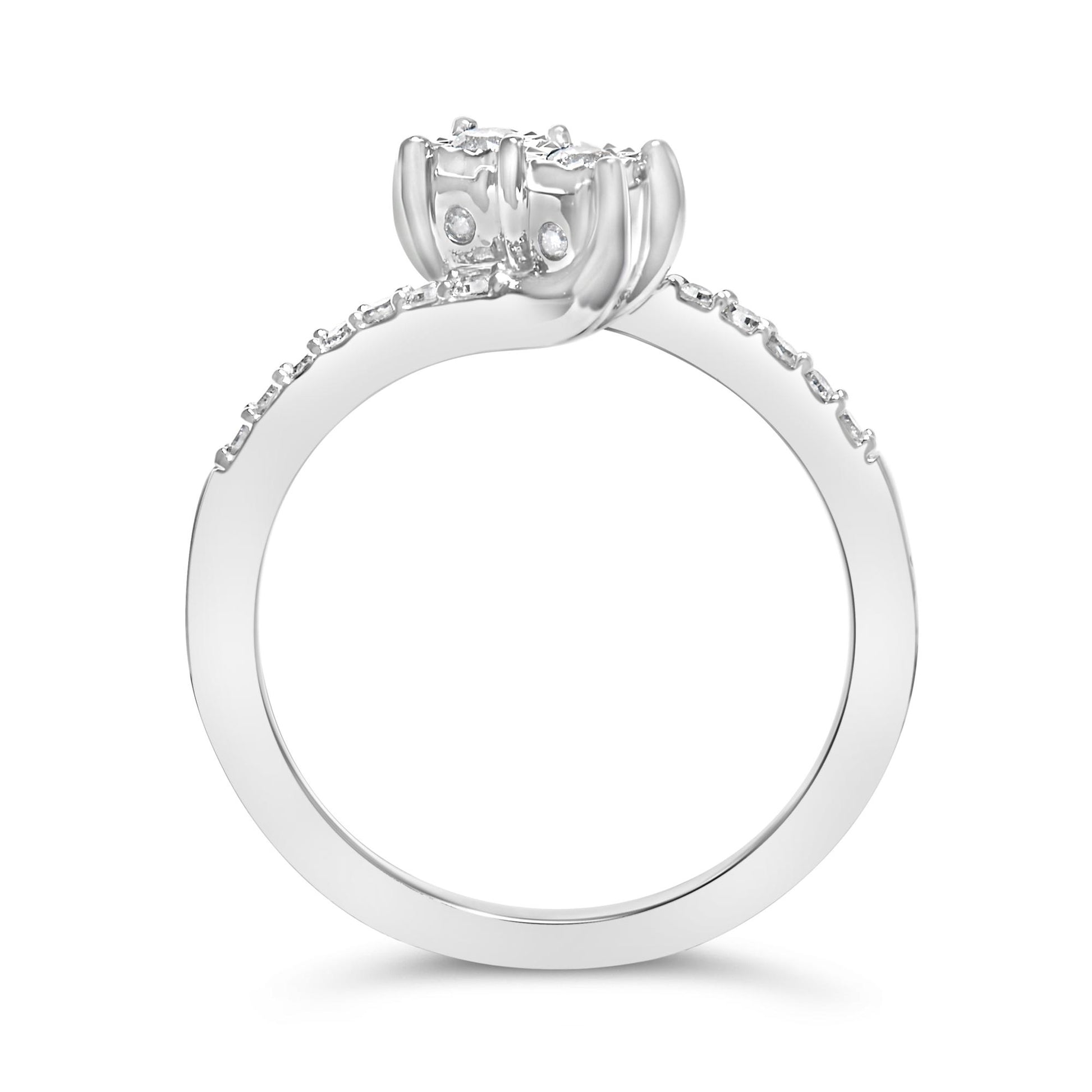 Close-up of a white metal ring shown from the side angle, featuring two round white gemstones in miracle settings at the center and multiple smaller round white gemstones in shared prong settings along the band.