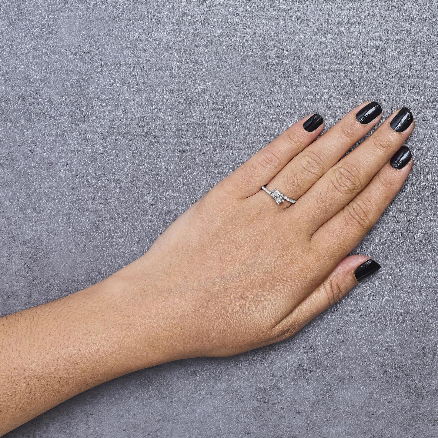 White metal ring with two larger white gemstones in miracle setting and multiple smaller white gemstones in shared prong setting, shown worn on a model's finger, captured from a top angle.