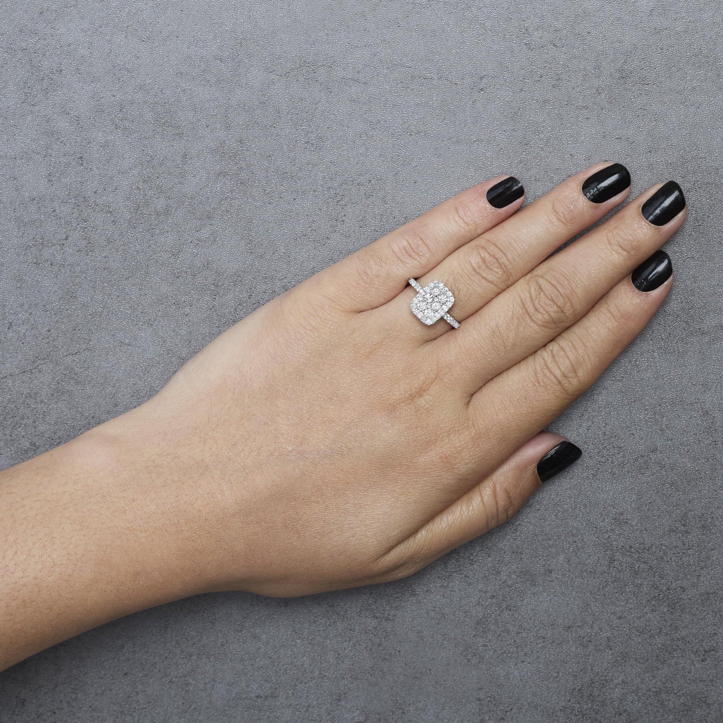 White metal ring with a cluster of round white gemstones in prong settings on a model's hand, shown from above.
