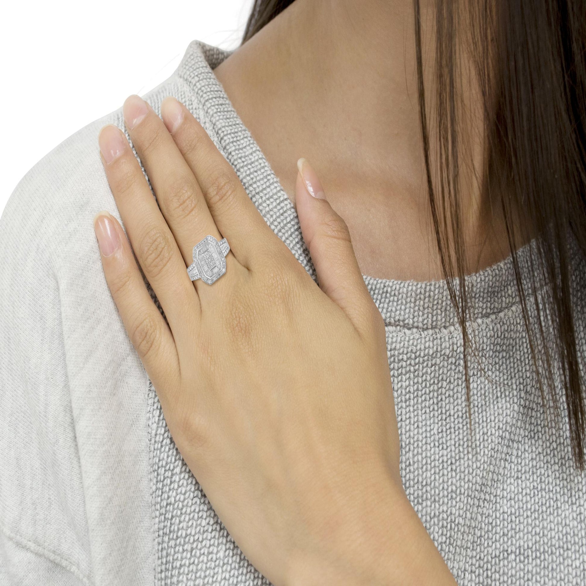 Close-up top angle of a white metal ring with round prong-set white gemstones surrounding a center cluster and baguette channel-set white gemstones on the band, worn on a model's hand.