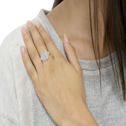 Close-up top angle of a white metal ring with round prong-set white gemstones surrounding a center cluster and baguette channel-set white gemstones on the band, worn on a model's hand.