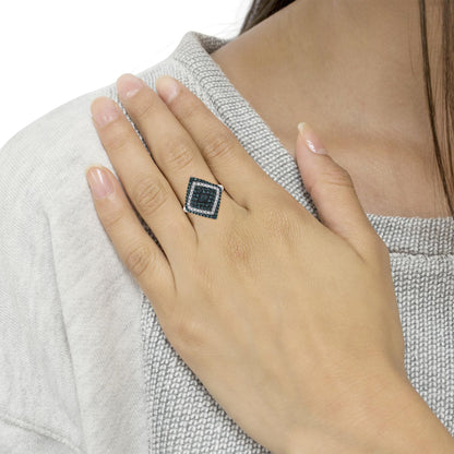 White metal ring with a square top featuring round blue and white gemstones in prong settings, shown on a model's hand from a top angle.