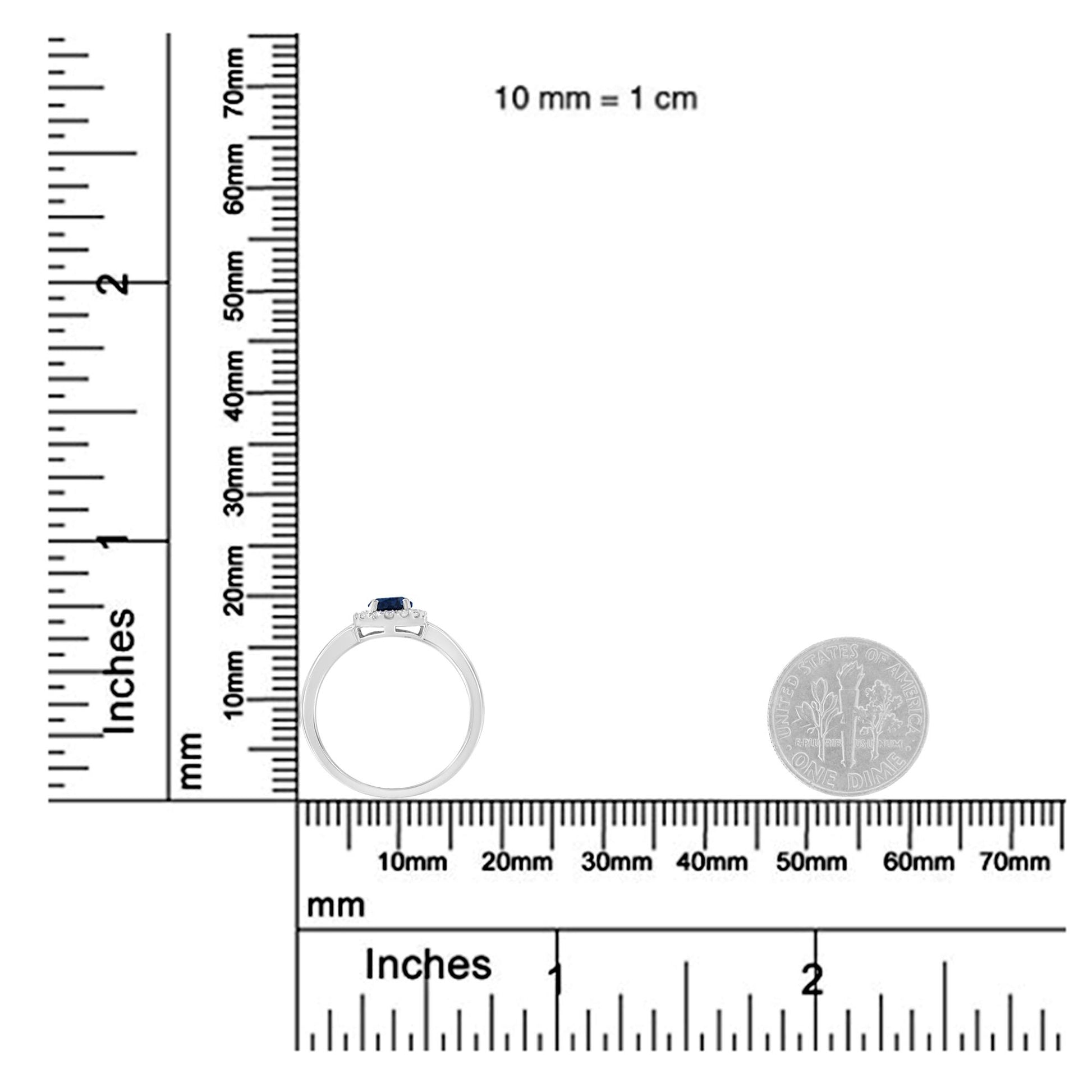 White metal ring with a blue oval gemstone center and multiple small white round gemstones around it in prong settings, shown from the side on a ruler and scale for size reference.