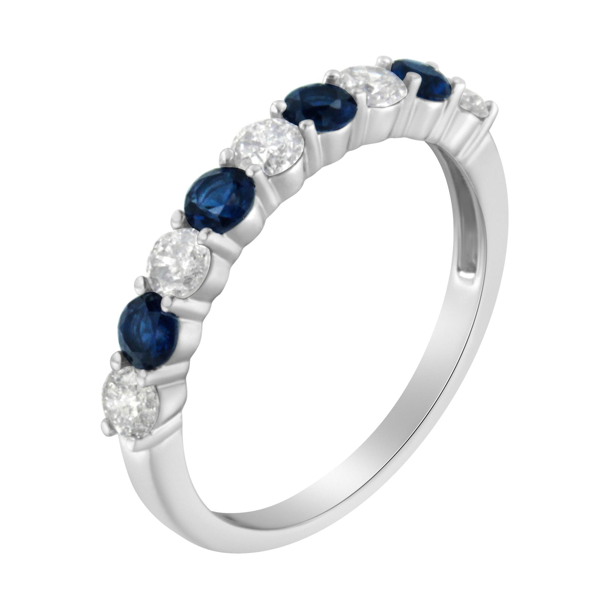 White metal ring with alternating round white and blue gemstones in prong settings, shown at an angle.