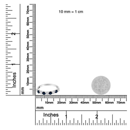 White metal ring with alternating round blue and white gemstones in prong settings, shown on a ruler and scale for size reference, front angled view.
