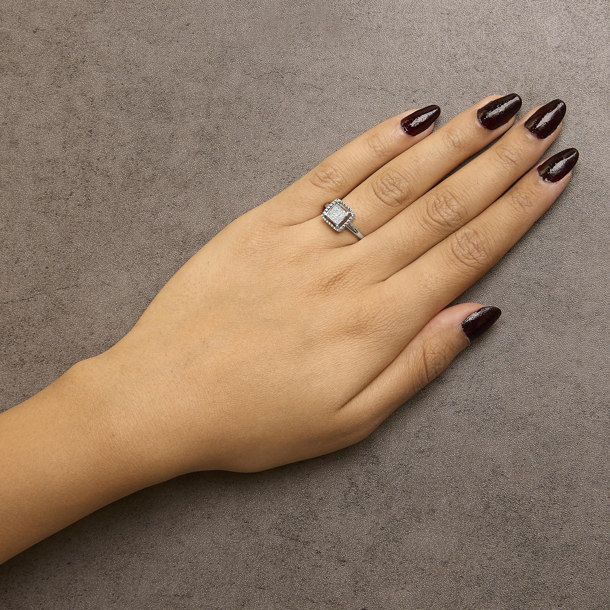 White metal ring with a princess-shaped white gemstones in an invisible setting, shown on a model’s hand from above.