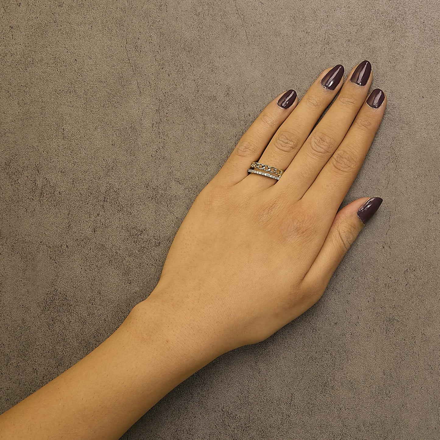 Top view of a yellow ring with round white gemstones in a shared prong setting on a model's ring finger, paired with a chain-link band.