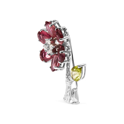 Side angled view of a white metal brooch shaped like a flower with pink oval gemstones forming petals, a cluster of small white round gemstones at the center, and a green pear-shaped gemstone on the stem.
