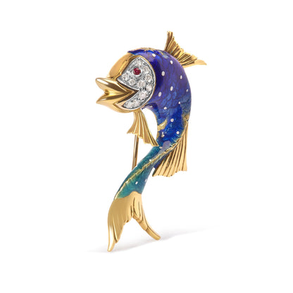 Yellow metal fish-shaped brooch with blue and green enamel and white and red gemstones on the face, shown from a front side angle.