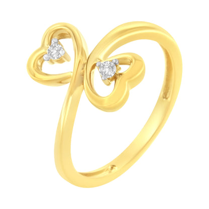 Yellow metal ring with two heart shapes open at the top, each set with a round prong-set white gemstone, shown from a slightly angled front view.