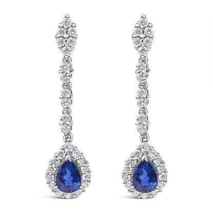 Front view of a pair of white metal drop earrings with round white gemstones in 4-prong settings along the length and a pear-shaped blue gemstone surrounded by round white gemstones at the bottom.