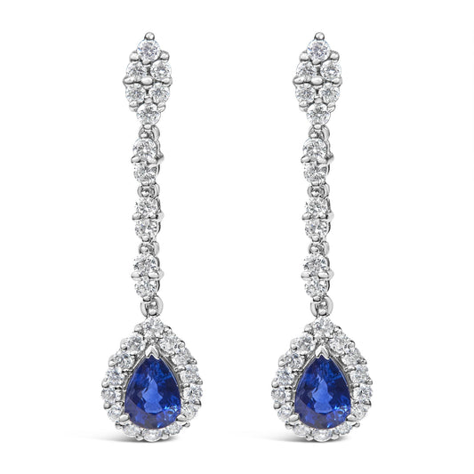 Front view of a pair of white metal drop earrings with round white gemstones in 4-prong settings along the length and a pear-shaped blue gemstone surrounded by round white gemstones at the bottom.