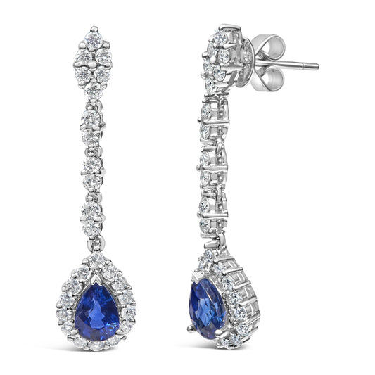 Front and side view of a pair of white metal drop earrings with round white gemstones set along the length and a pear-shaped blue gemstone surrounded by round white gemstones at the bottom.