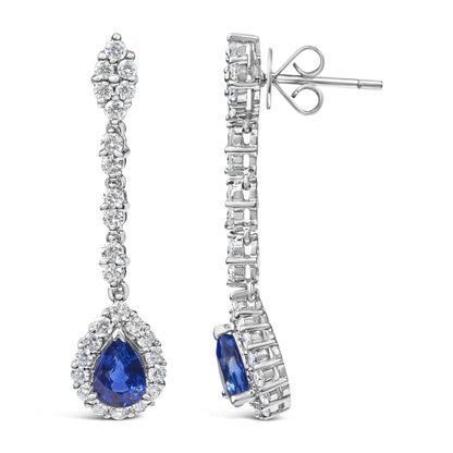 Front and side views of white metal drop earrings with round white gemstones in prong settings and pear-shaped blue gemstones surrounded by round white gemstones, shown against a white background.