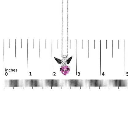 Necklace shown on a scale, photographed from the front, featuring a white and black metal angel pendant with a heart-shaped pink gemstone and round white and black gemstones.