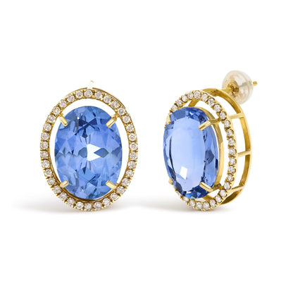 Close-up front and side angle of a pair of yellow metal earrings featuring large oval blue gemstones in 4-prong settings, surrounded by a halo of small round white gemstones in prong settings, shown on a white background.