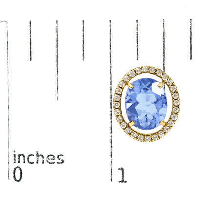 Close-up angled view of a yellow metal earring featuring an oval blue gemstone in a four-prong setting, surrounded by a halo of small round white gemstones in prong settings, shown on a measurement scale.