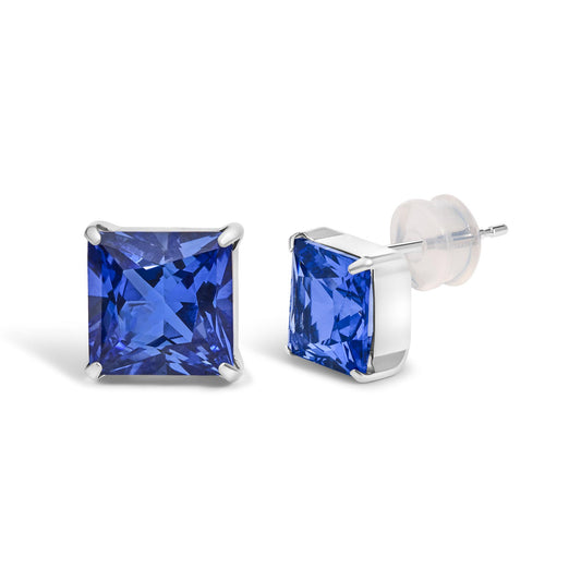 Close-up front and side angle of a pair of white metal stud earrings with princess-shaped blue gemstones in a four-prong setting.