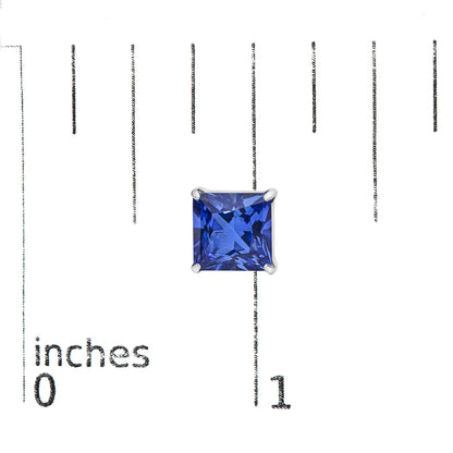 Close-up front view of a single white metal earring featuring a princess-shaped blue gemstone in a four-prong setting, shown on a measurement scale.