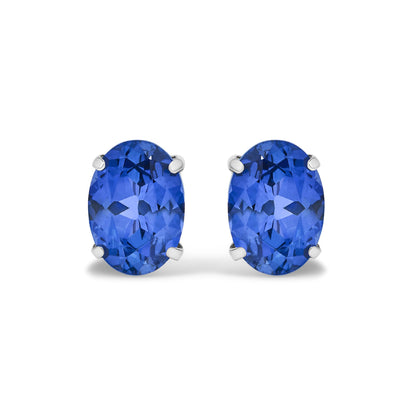Close-up front view of white metal earrings, each featuring an oval blue gemstone in a four-prong setting.