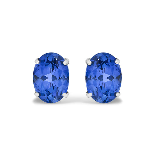 Close-up front view of white metal earrings, each featuring an oval blue gemstone in a four-prong setting.