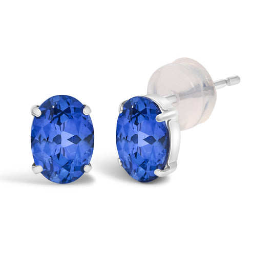 Close-up angled view of white metal stud earrings with oval-shaped blue gemstones in four-prong settings.