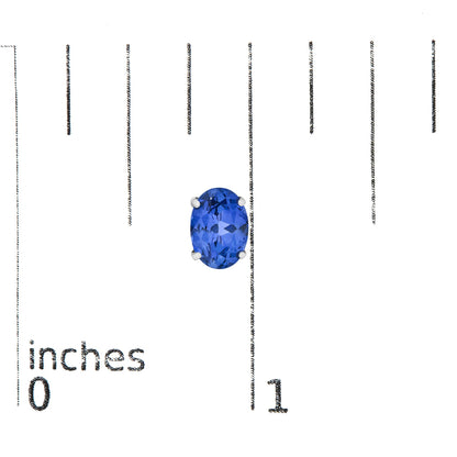 Close-up front angle of white metal earrings featuring oval blue gemstones secured in 4-prong settings, shown on a measurement scale.