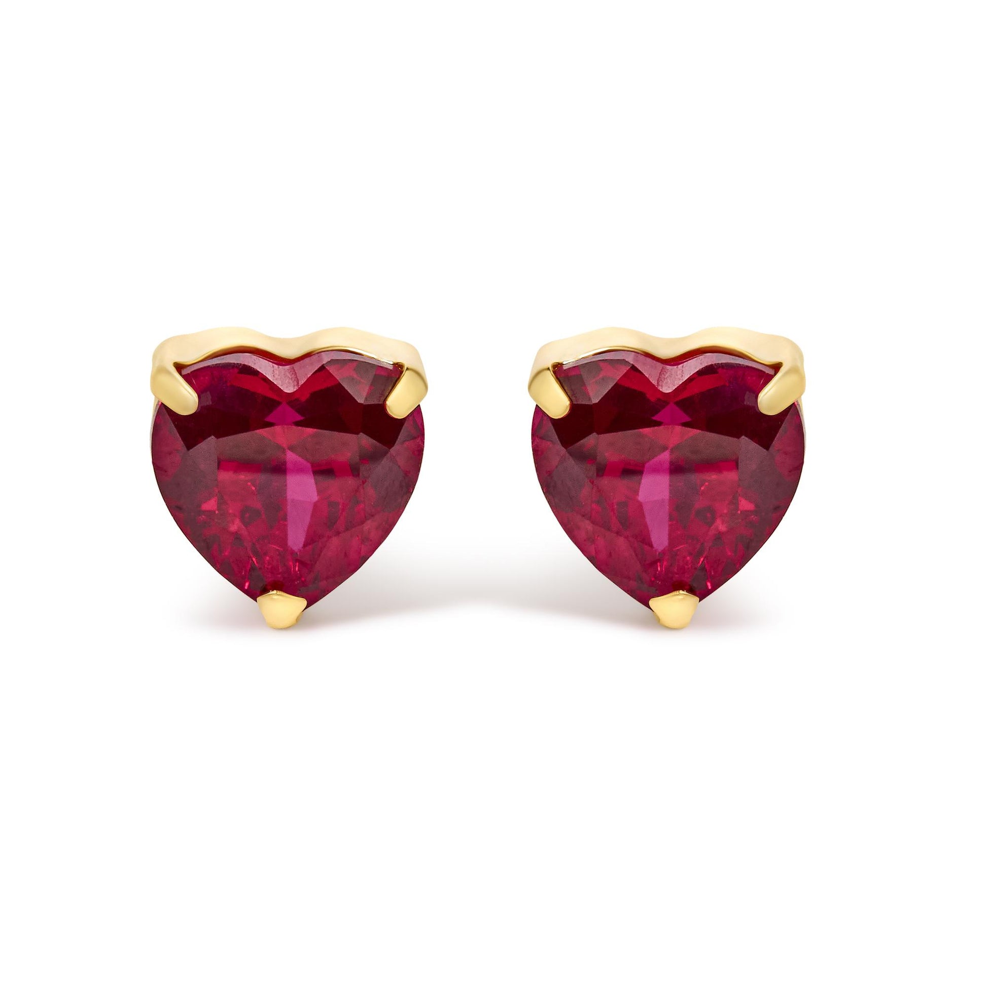 Close-up front view of yellow metal heart-shaped earrings featuring red heart-shaped gemstones in three-prong settings.