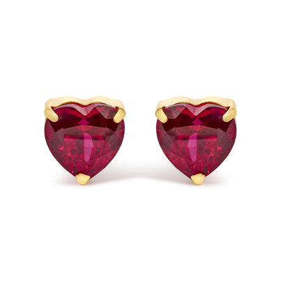 Close-up front view of yellow metal heart-shaped earrings featuring red heart-shaped gemstones in three-prong settings.