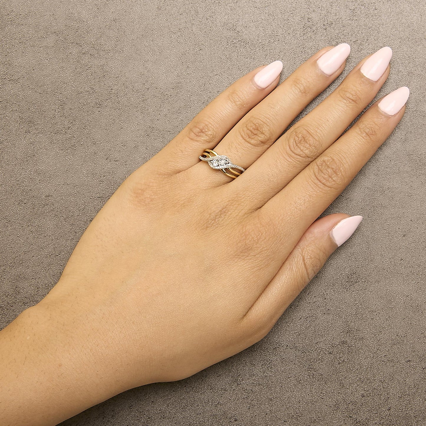 Ring with intertwined yellow and white metal bands, featuring round white gemstones in prong settings, shown worn on a model's finger from a top angle.