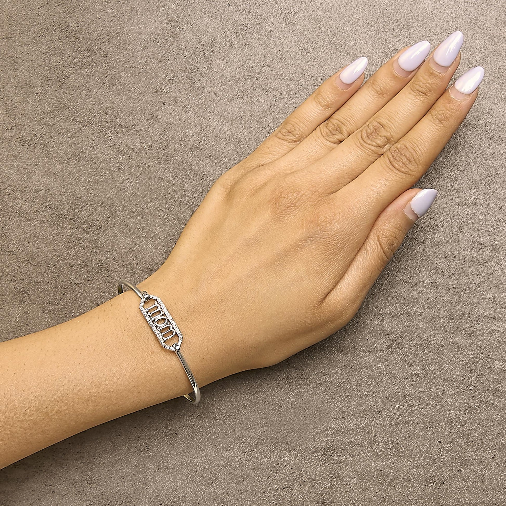 White metal bracelet with a rectangular centerpiece adorned with round white gemstones in prong settings, shown on a model's wrist from a top-down angle.