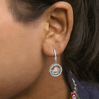 Close-up side view of a model wearing a round, white and rose metal earring with a circular design featuring white gemstones and a small rose-colored heart in the center.