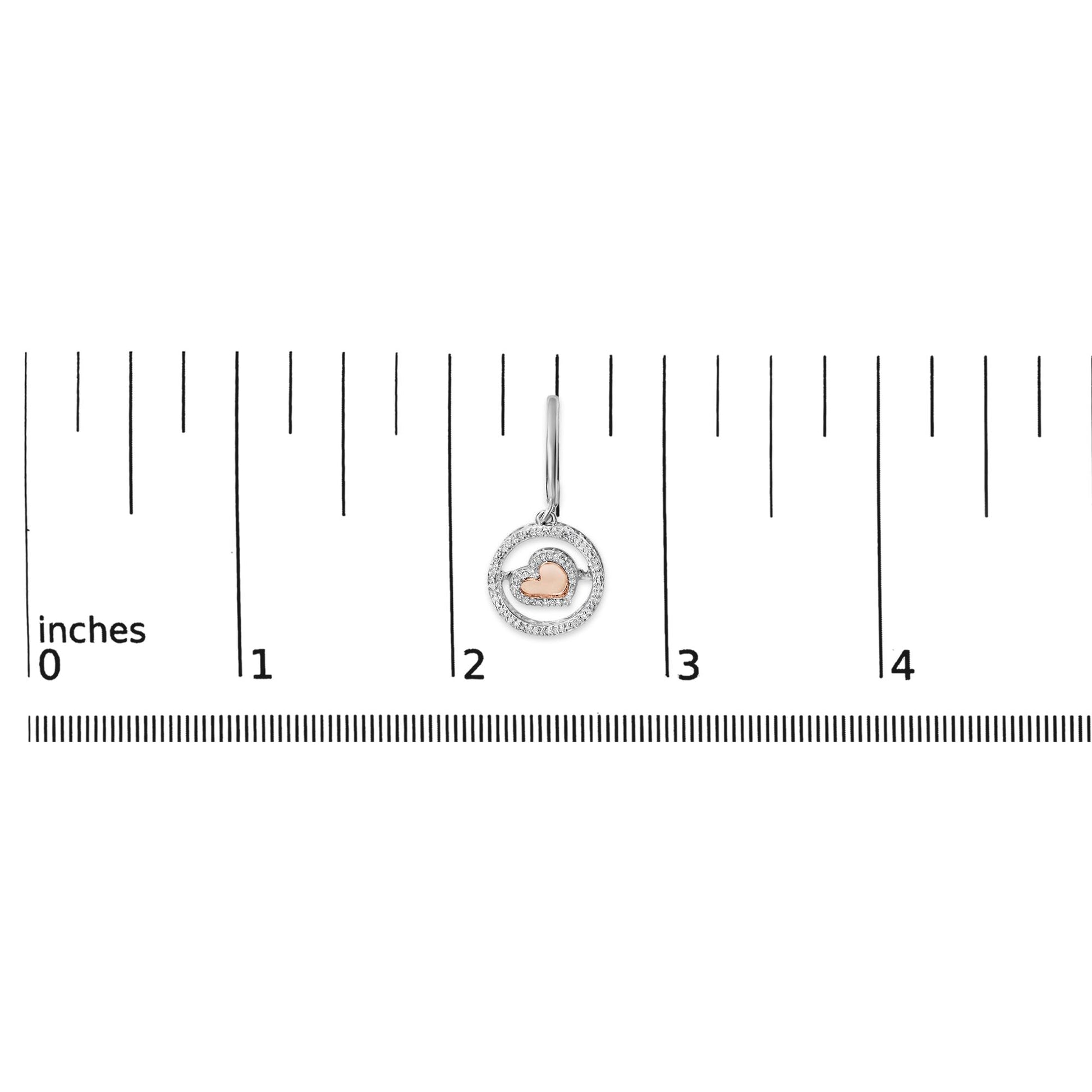 Earring with a rose heart shape surrounded by two concentric white metal circles set with round white gemstones, shown on a ruler scale from a front angle.