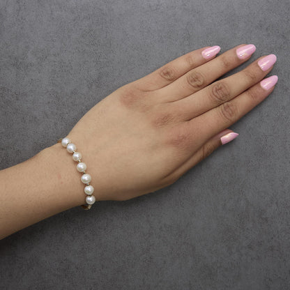 Yellow metal bracelet with white round gemstones, shown worn on a model's wrist in a top-down angle.