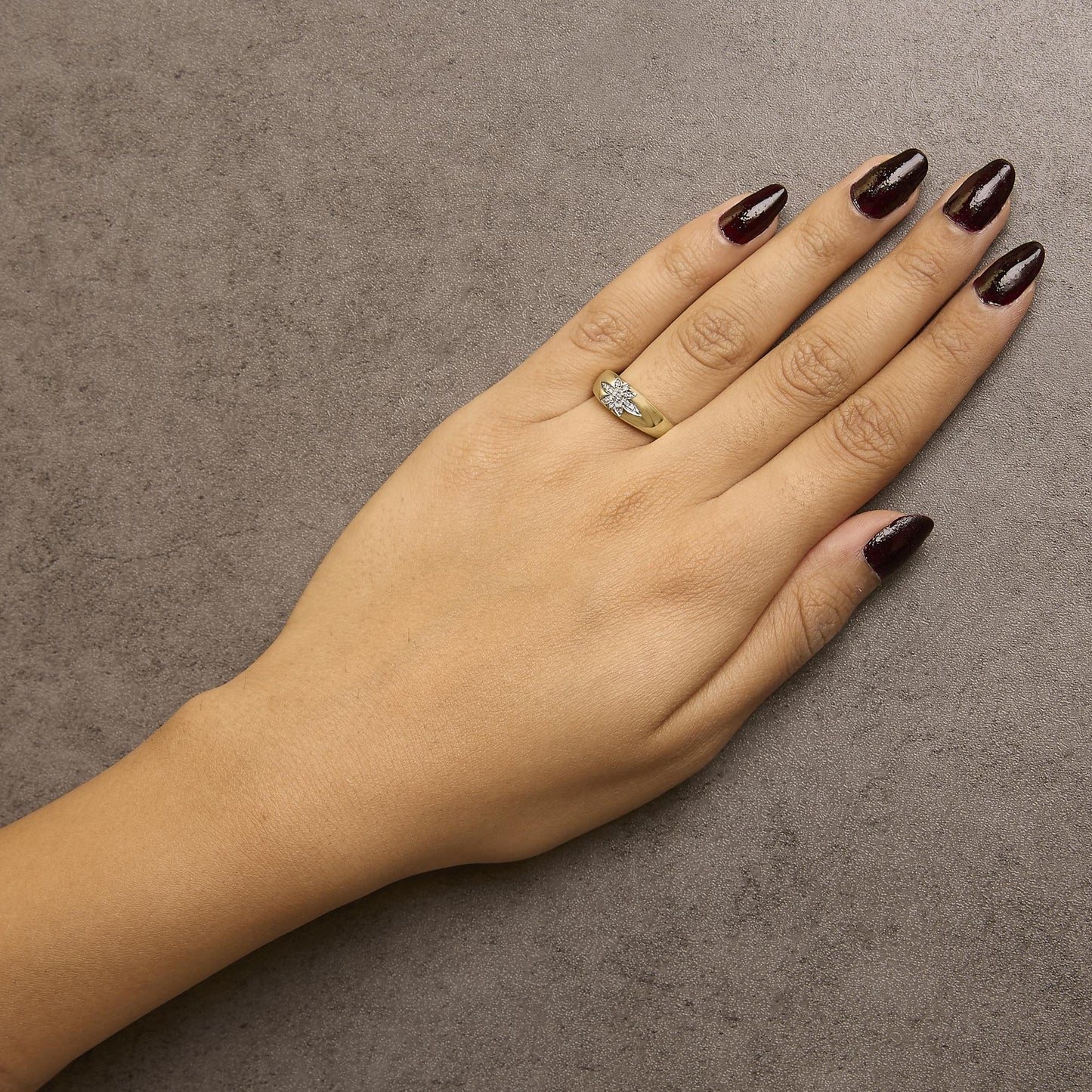 Yellow metal ring with round white gemstones in prong settings, shown worn on a model's hand, top angle.