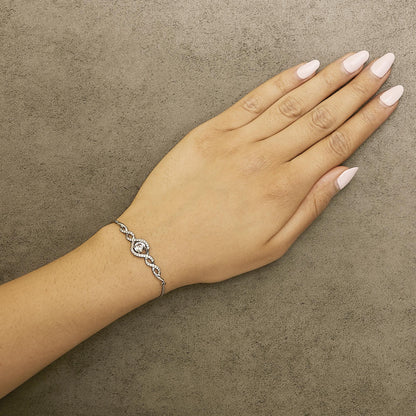 White metal bracelet with intertwined loop design and multiple round white gemstones, shown on a model's wrist from a top angle.