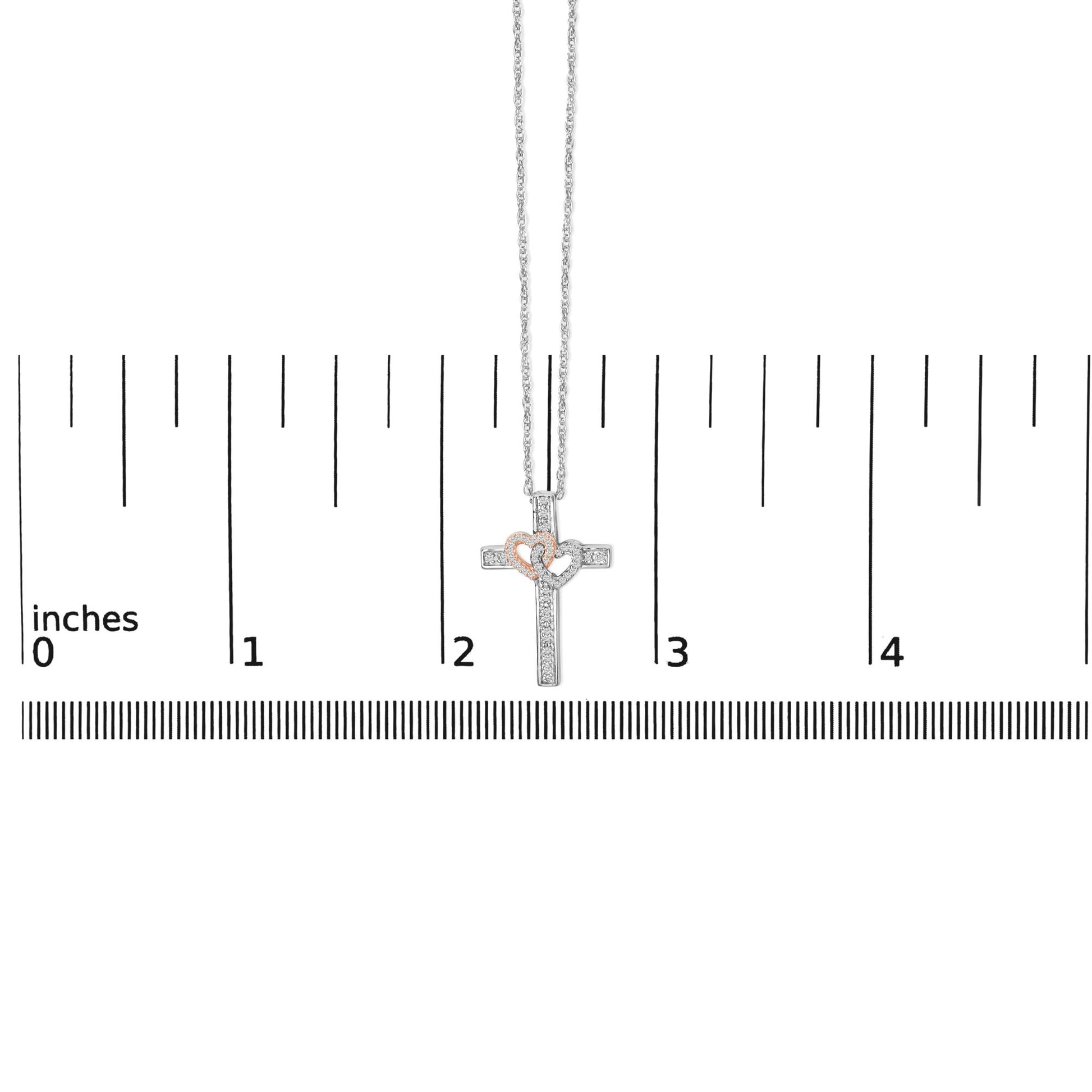 Necklace shown on a scale, featuring a cross pendant with two overlapping hearts; the cross and one heart are white metal with white gemstones in a pave setting, and the other heart is rose metal with white gemstones, front view.