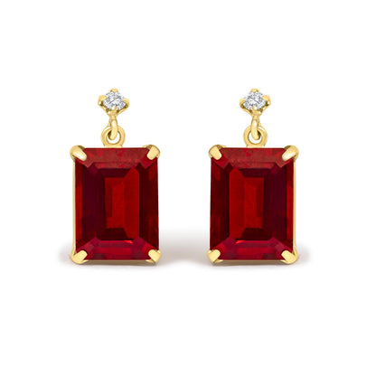 Close-up front view of yellow metal earrings with red emerald-shaped gemstones and white round gemstones held in 4-prong settings.