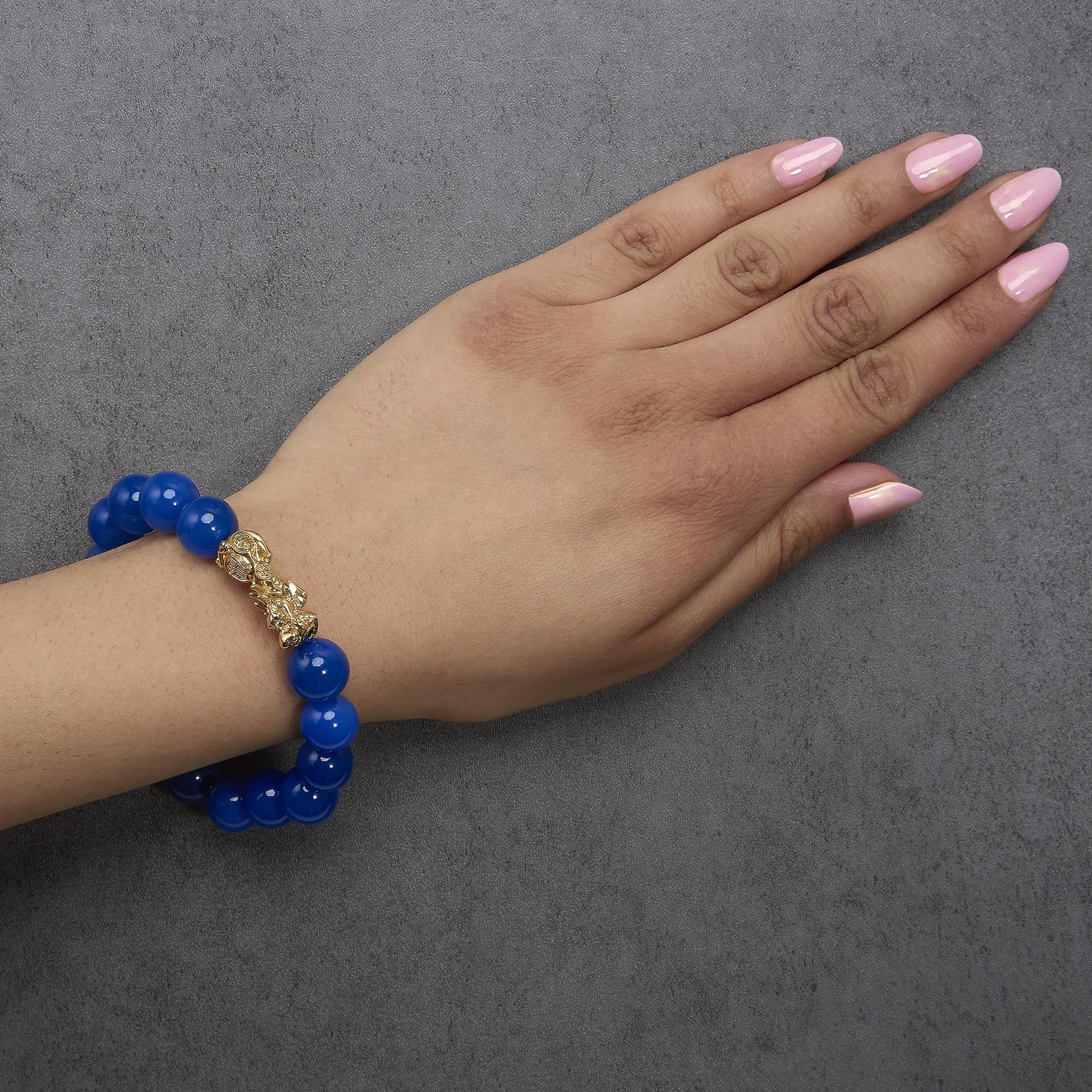 Yellow metal bracelet with round blue gemstones and decorative accents, shown worn on model's wrist from an angled top view.