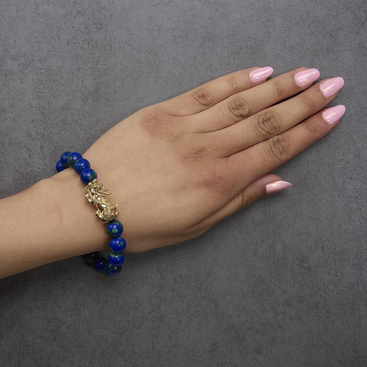 Bracelet with round blue gemstones and a yellow metal charm, shown worn on a model's wrist from a top angle.