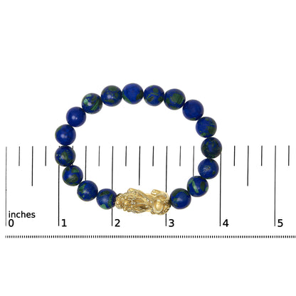 Close-up front view of a yellow metal bracelet with round blue and green gemstones in a drilled setting, shown on a scale.
