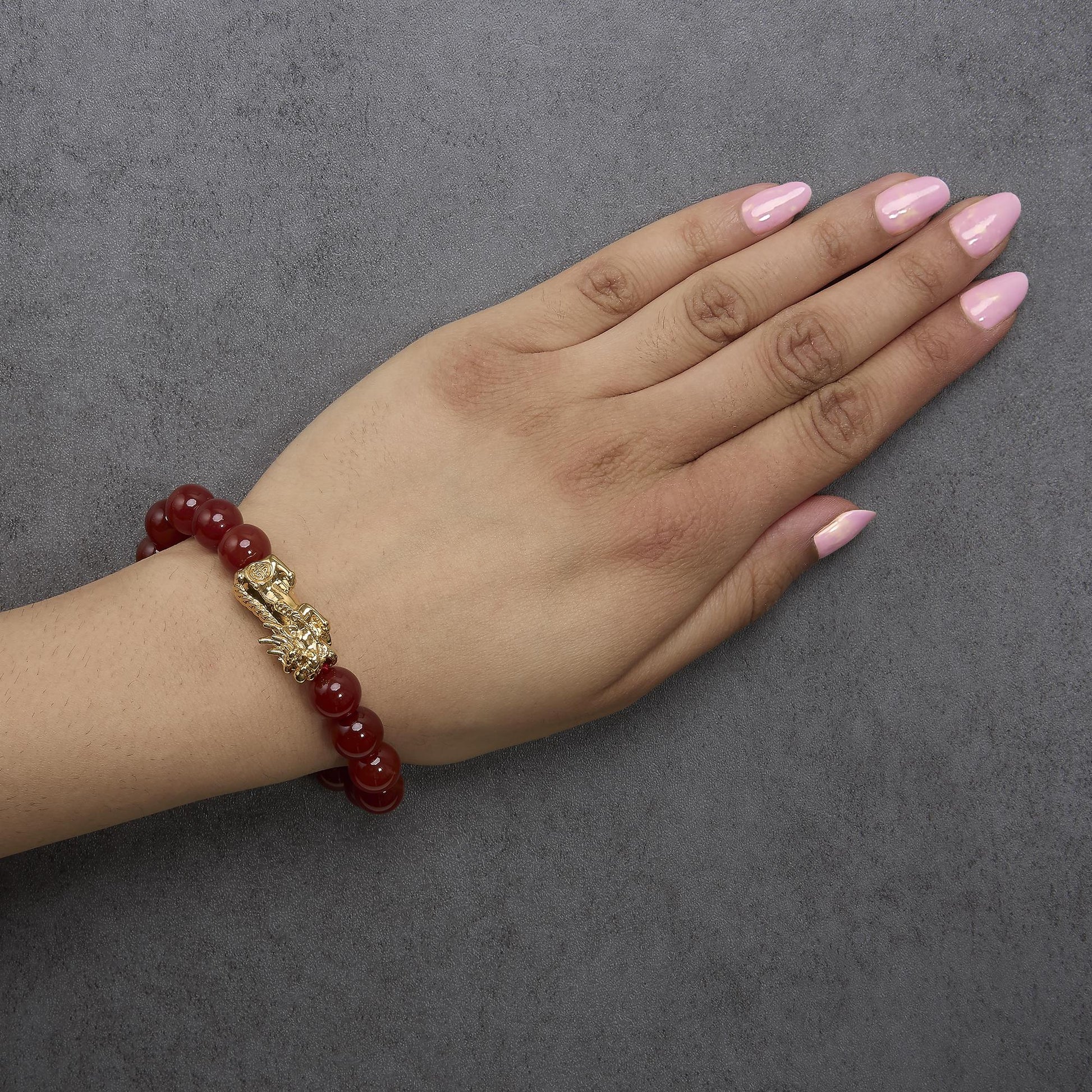 Yellow metal bracelet with round red gemstones and a decorative yellow metal element, shown worn on a model's wrist from a top angle.