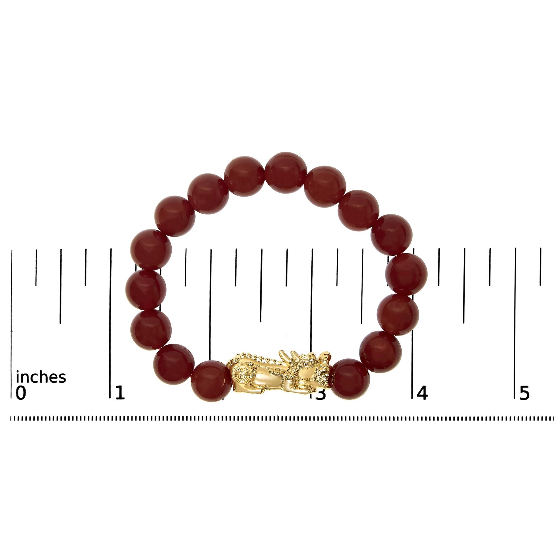 Top-down view of a yellow metal bracelet featuring round red gemstone beads and a dragon-shaped clasp, displayed on a scale.