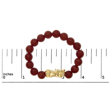 Top-down view of a yellow metal bracelet featuring round red gemstone beads and a dragon-shaped clasp, displayed on a scale.