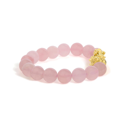 Close-up front angle of a yellow metal bracelet with round pink gemstone beads and a detailed gold-colored charm, shown on a white background.