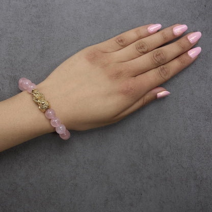 Close-up of a model's wrist and hand shown from the top angle wearing a bracelet made of round pink gemstones with yellow decorative metal accents.