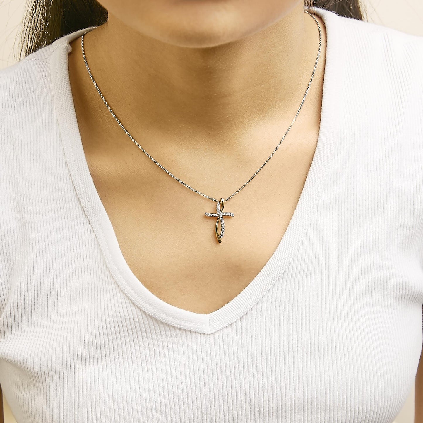 Necklace with an intertwined cross pendant featuring yellow and white metal colors and round white gemstones in prong settings, shown worn on a model from a front angle.