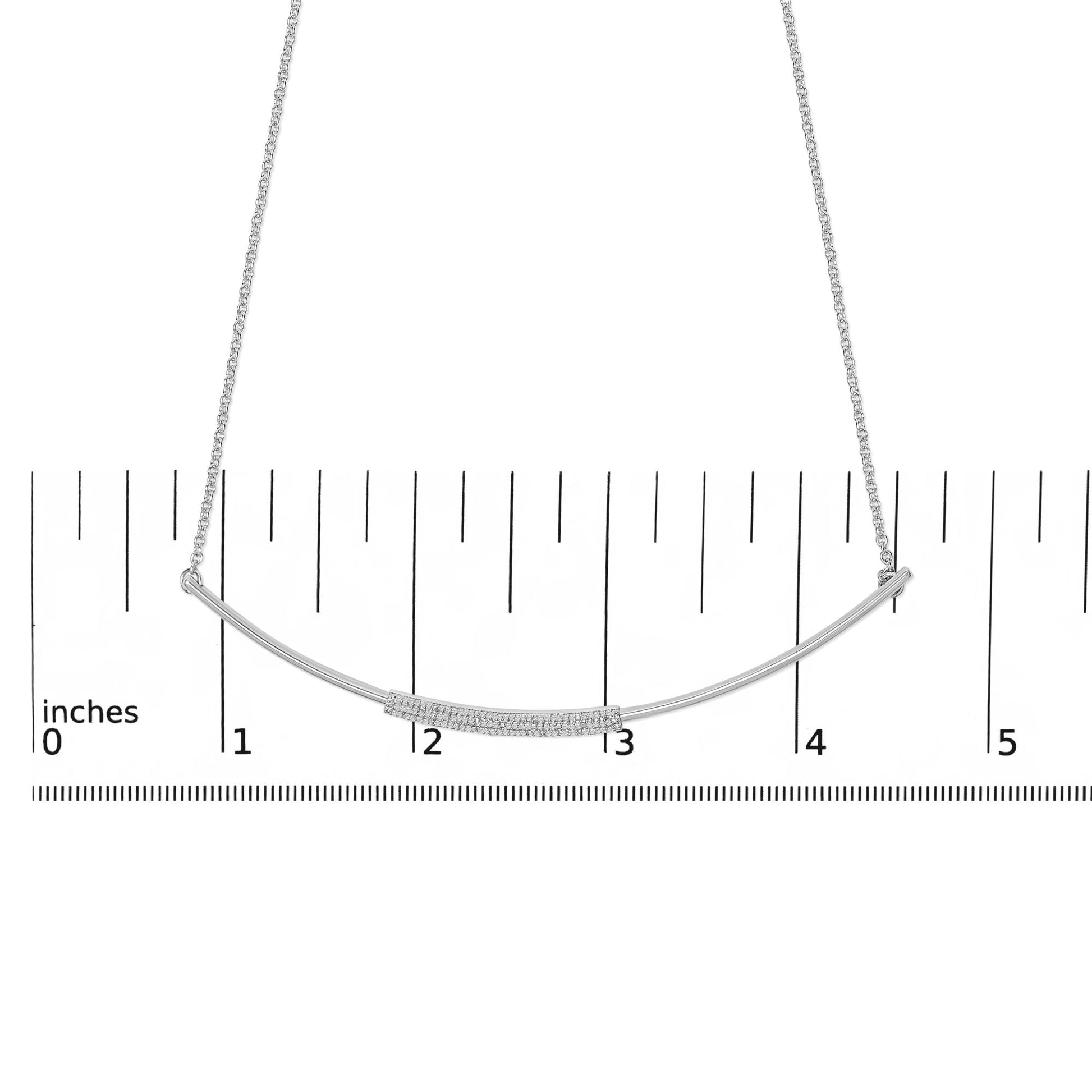 White necklace with a curved bar pendant set with small white gemstones in a pave setting, shown on a ruler for scale, front-facing angle.