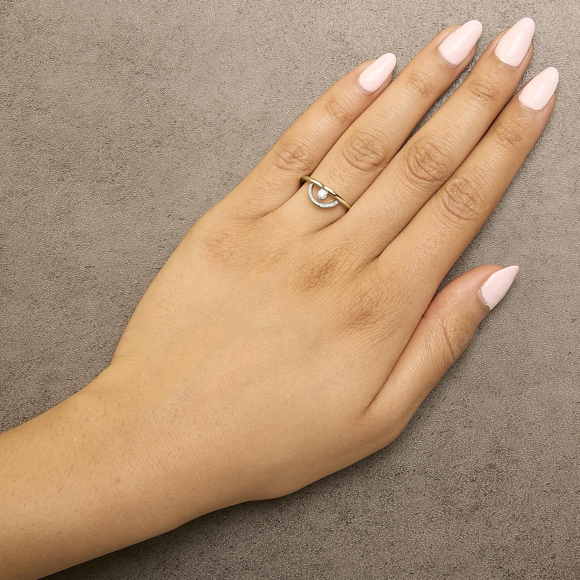Ring with yellow and white metal worn on a model's hand, featuring a round white gemstone in a three-prong setting and multiple smaller round white gemstones in a shared prong setting, shown from a top angle.