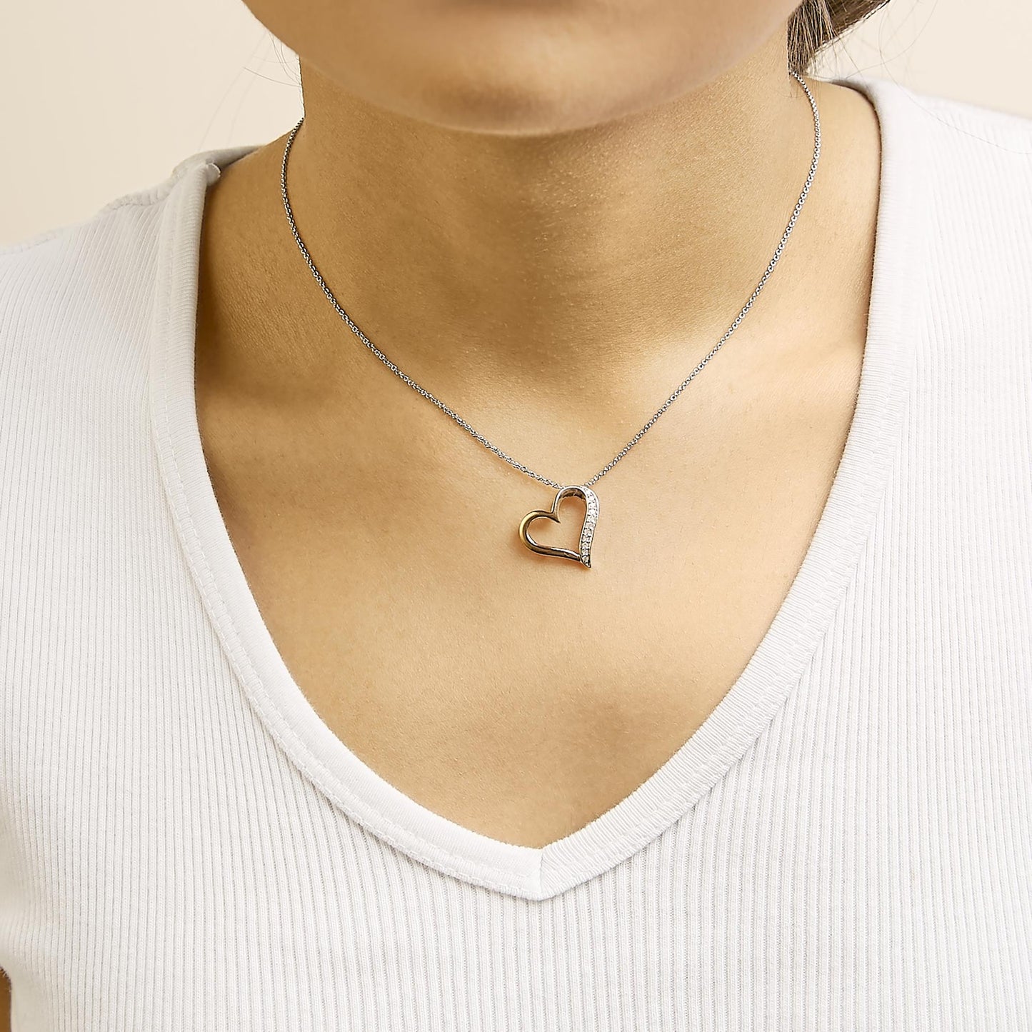 Necklace shown worn on a model, featuring a heart-shaped pendant with white and rose metal colors, adorned with white round pave-set gemstones on one side, shot from the front.